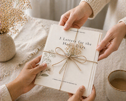 Two hands holding a book titled '3 Letters for the Heavy Days' with decorative elements on a soft surface.
